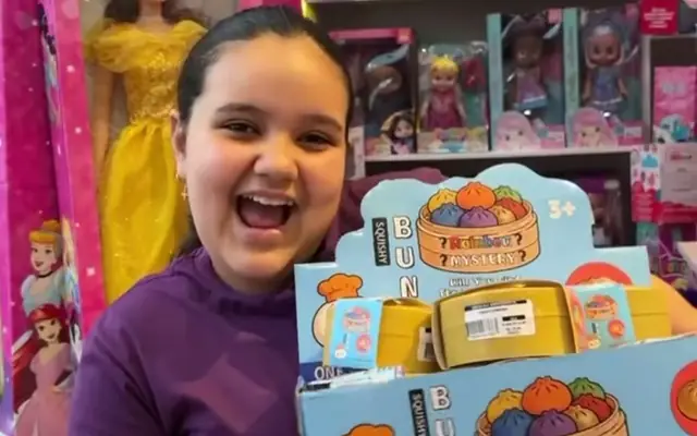 Menina mostrando um brinquedo de coleção entre as prateleiras